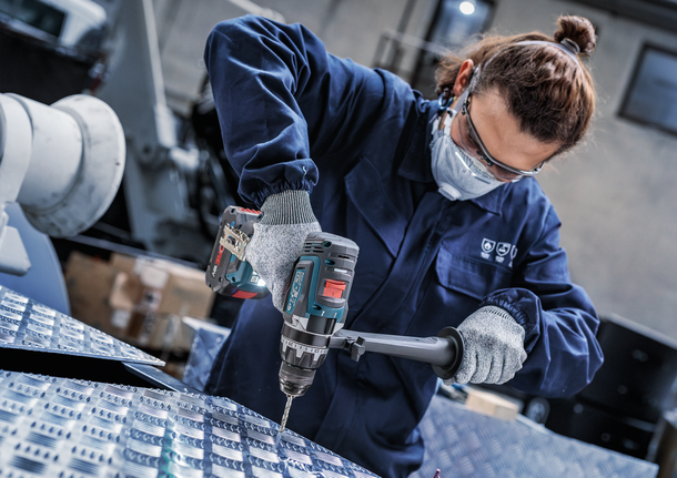 Person wearing safety equipment drills into a metal plate.