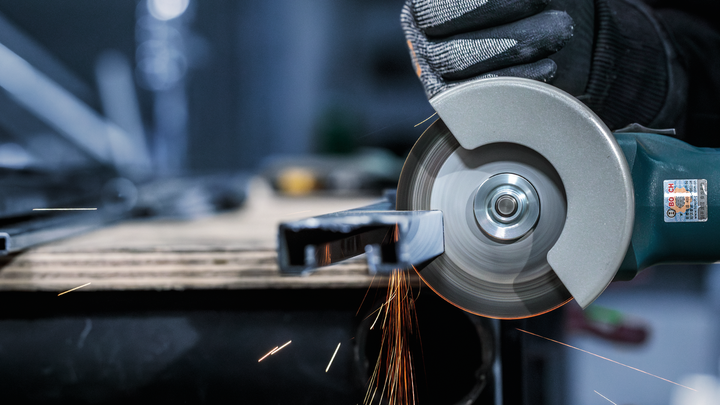 Person wearing safety equipment uses an angle grinder to cut metal, creating sparks.