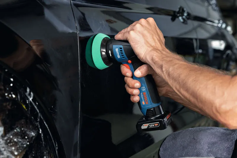 A person uses a cordless polisher to buff the surface of a black car door.