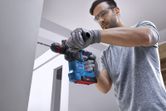 A person wearing safety equipment drills into a concrete wall using a cordless rotary hammer.
