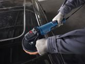 A person wearing safety equipment polishes a car roof with a power polisher.