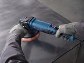 A person wearing safety equipment uses a polisher on a metal surface.