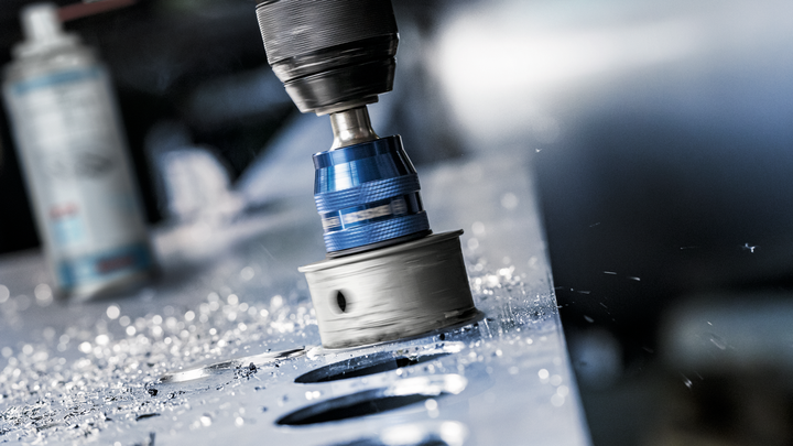 Hole saw drilling circular holes in a metal sheet, with metal shavings scattered around.