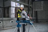 Person wearing safety equipment operates a metal cut-off saw on a construction site.