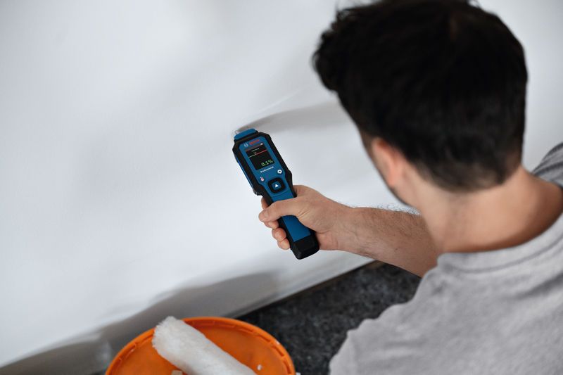 Person checks wall moisture with a material moisture meter in a freshly painted room.