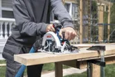 A person cuts a wooden board with a cordless circular saw at a construction site.