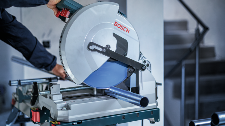 Person wearing safety equipment cuts a metal pipe with a circular saw.