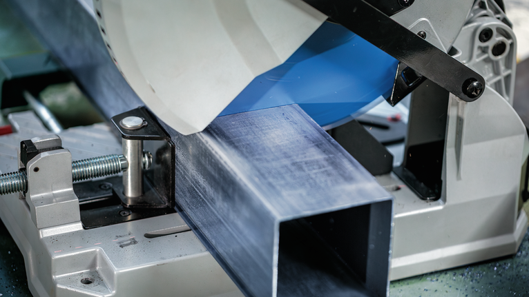 Metal cutting saw slices through a large steel beam in an industrial setting.