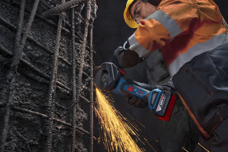 A person wearing safety equipment uses an angle grinder to cut steel rebar.