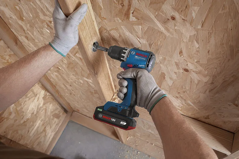 A person wearing safety equipment drills a screw into a wooden panel.