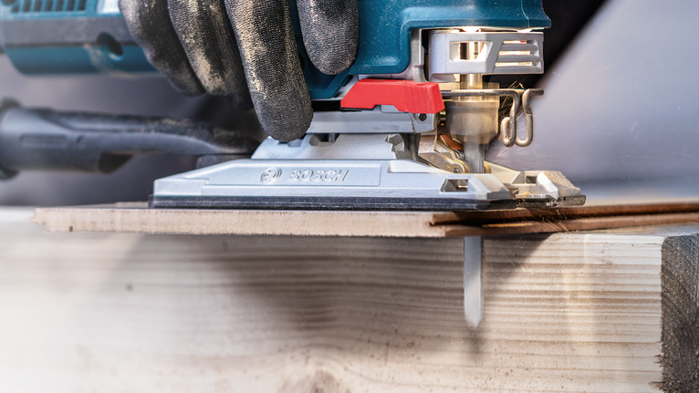 Person wearing safety equipment guides a jigsaw to cut a wooden board.