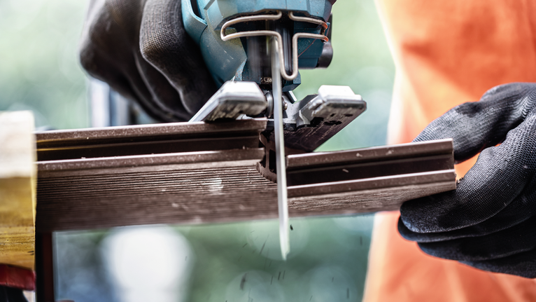 Person wearing safety equipment uses a jigsaw to cut a metal rail.