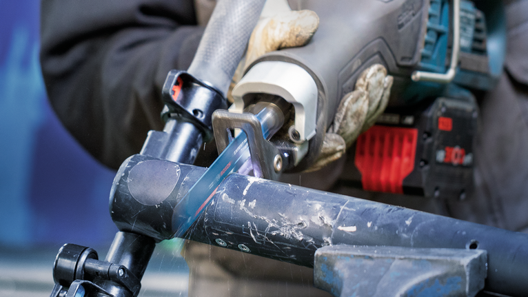 Person wearing safety equipment uses a reciprocating saw to cut a metal pipe.