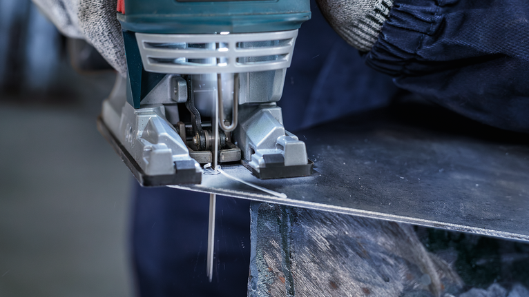 Person wearing safety equipment cuts a metal sheet with a jigsaw.