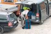 A person loading stacked toolboxes onto a collapsible hand truck beside a van.