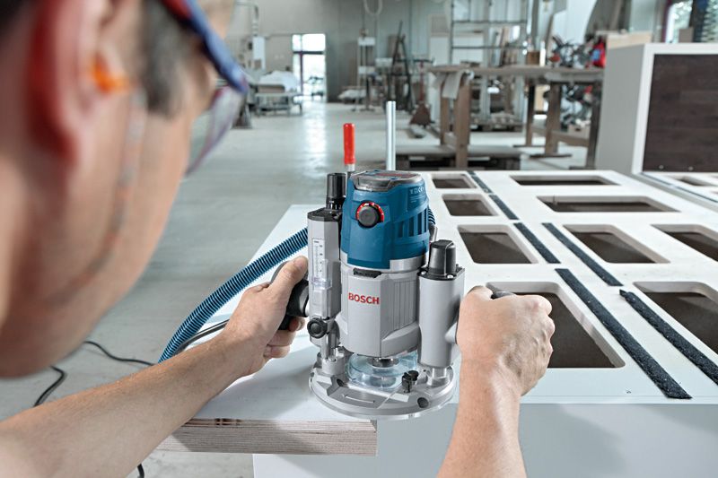 A person wearing safety equipment uses a router to shape the edge of a wooden board.