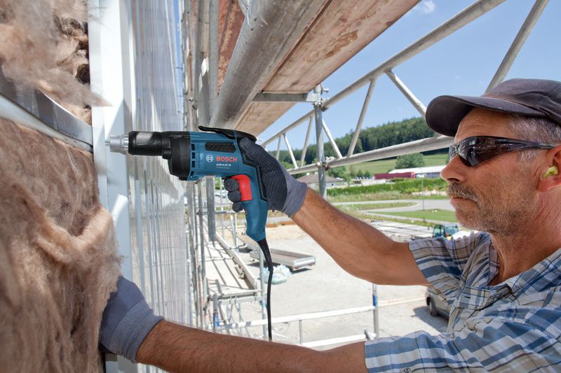 Person wearing safety equipment fastens drywall panels with a drywall screwdriver.