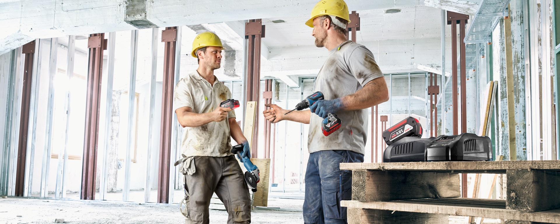 Два рабочих в касках держат инструменты на строительном объекте.