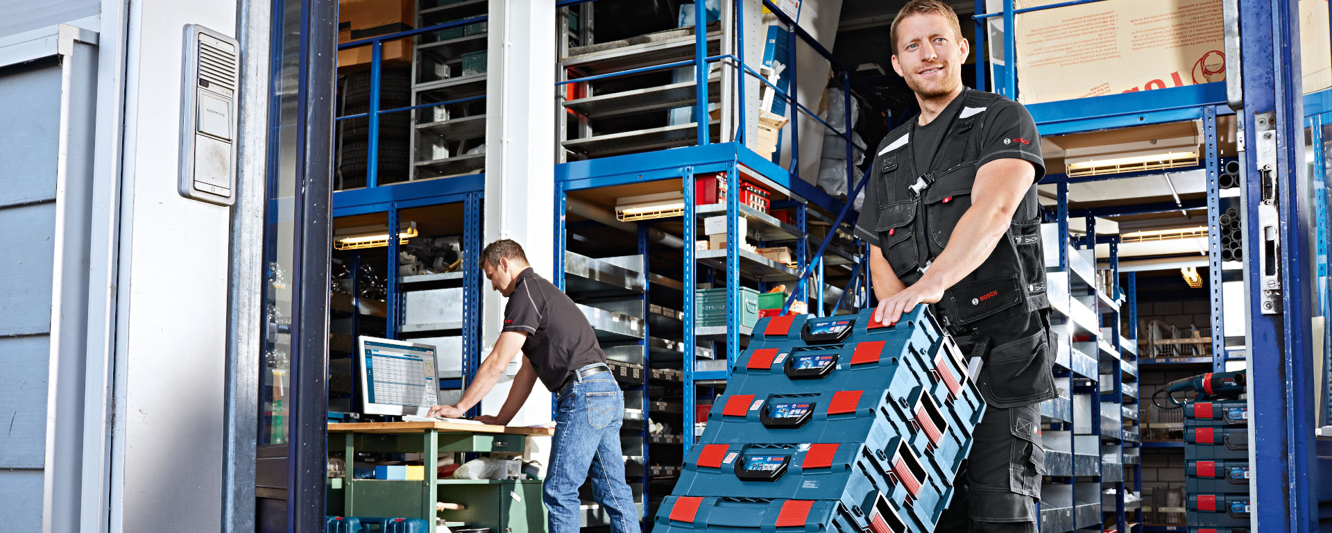 Рабочий с инструментами Bosch в складе, другой работает за компьютером.