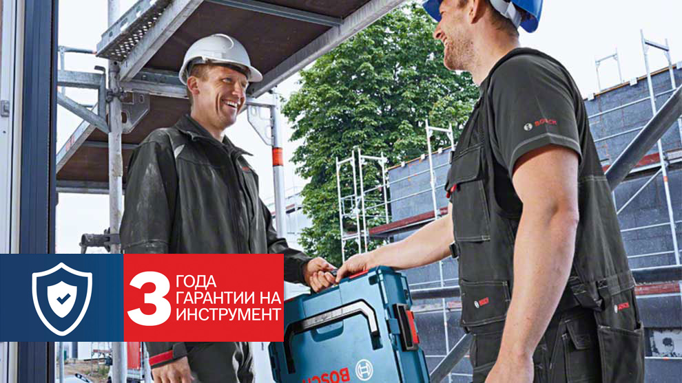 Два строителя улыбаются, передавая инструмент Bosch на строительной площадке.