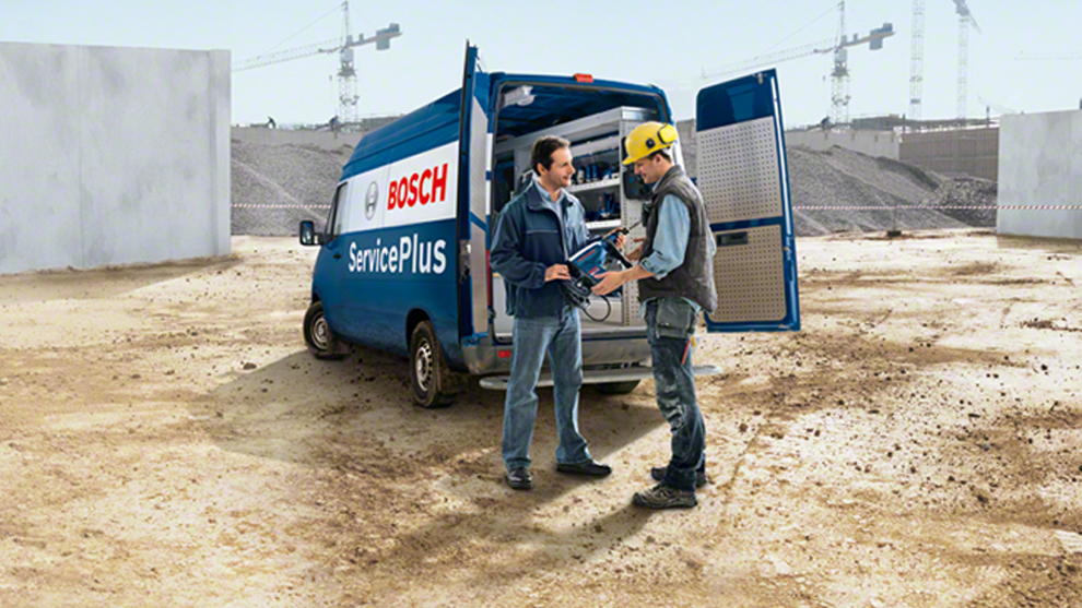 Два человека обсуждают инструменты у синего фургона Bosch на строительной площадке.