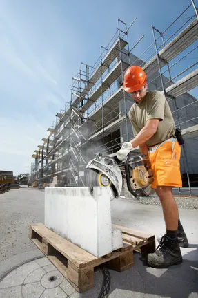 Человек в защитном снаряжении распиливает большой бетонный блок электропилой.