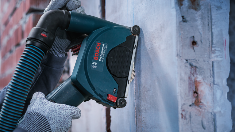 Человек, использующий средства индивидуальной защиты, управляет штроборезом по бетону.