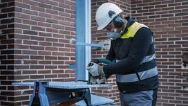 Человек в защитном снаряжении режет большую плитку циркулярной пилой.