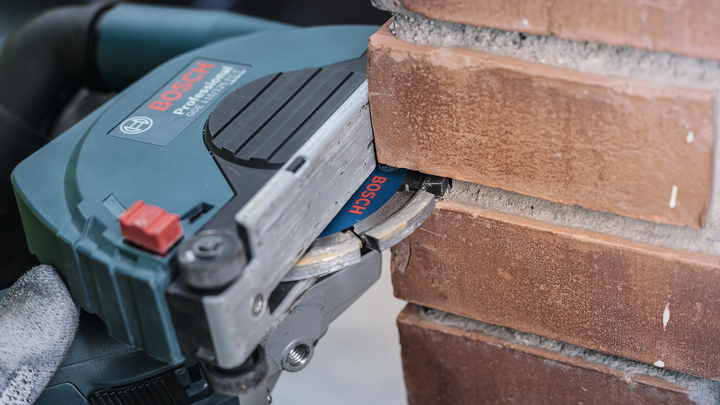 Человек в защитном снаряжении использует штроборез, чтобы прорезать канавку в кирпиче.