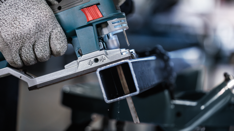 Человек в защитном снаряжении режет металлическую балку электролобзиком.