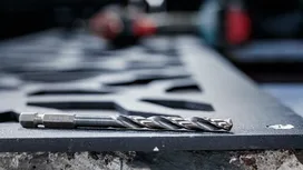 Металлическое сверло, лежащее на разрезанном стальном листе в мастерской.