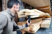 Человек измеряет влажность в штабелированных пиломатериалах с помощью цифрового влагомера.