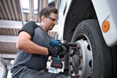 شخص يرتدي معدات السلامة يستخدم مفتاح ربط لاسلكي لربط مسامير عجلات الشاحنة.