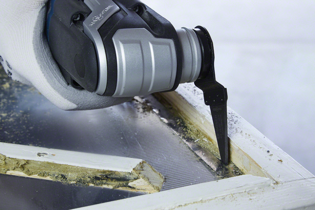 Gloved hand uses oscillating tool to cut old window frame putty.