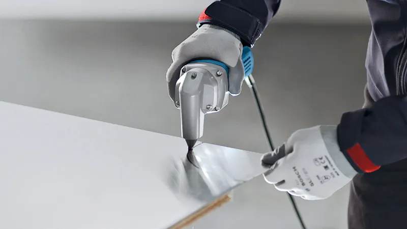 A person wearing safety equipment cuts sheet metal with a nibbler.