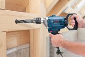 A person operates a power drill to bore a hole through a wooden beam.