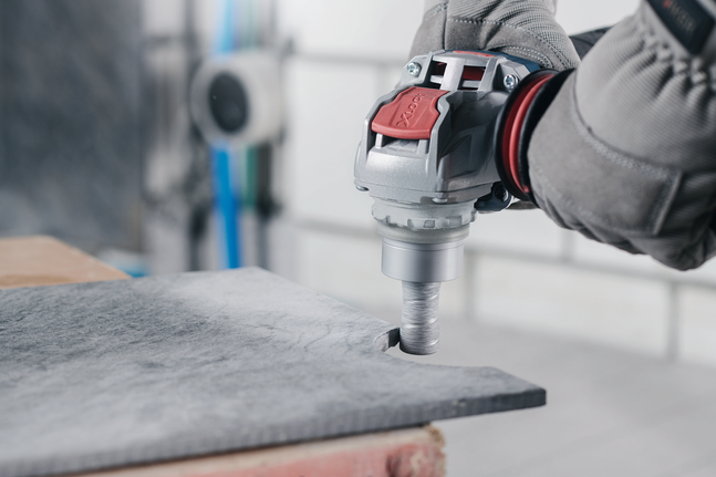 A person wearing safety equipment drills a circular hole in a stone slab.