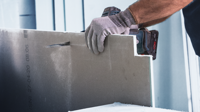 Person wearing safety equipment cuts drywall with a power tool.