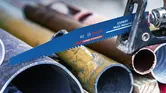 Reciprocating saw blade cutting through a metal pipe in a workshop setting.