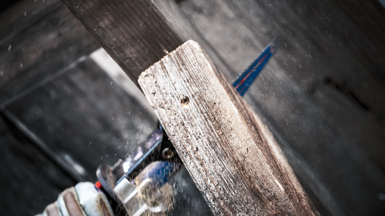 Person wearing safety equipment cuts a wooden plank with a reciprocating saw.