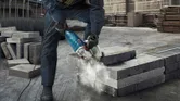 A person wearing safety equipment cuts concrete blocks with a power cutter.