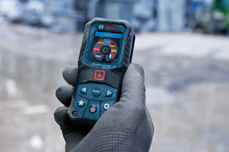 Person wearing safety equipment holds a laser measure displaying language options.