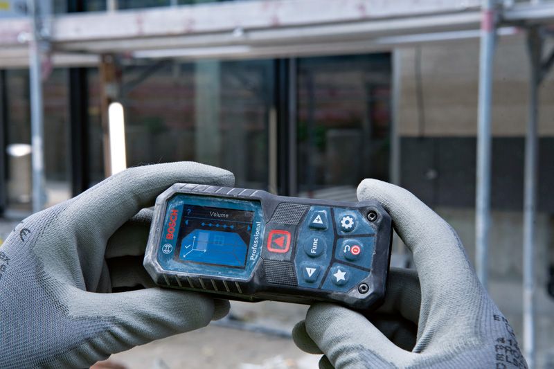 A person wearing safety equipment holds a laser measure at a construction site.