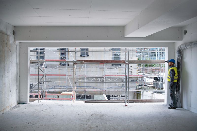 A person wearing safety equipment uses a laser measure inside a building under construction.