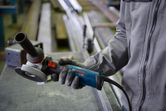 A person wearing safety equipment holds an angle grinder in a workshop.