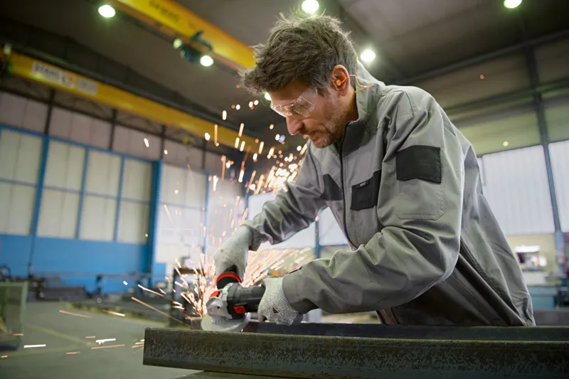 A person wearing safety equipment uses an angle grinder with X-LOCK on metal.