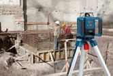 A person wearing safety equipment uses a laser leveling tool at a construction site.