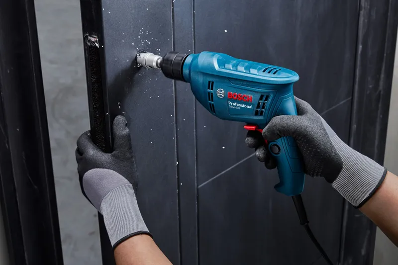 A person wearing safety equipment drills a hole into a metal wall with a power tool.