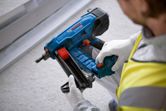 A person wearing safety equipment loads nails into a blue cordless concrete nailer.