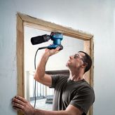 A person wearing safety equipment drills into a wooden door frame with a power tool.